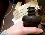 Hand holding base of wooden furniture foot with large wooden screw adorned with paper tag on top.